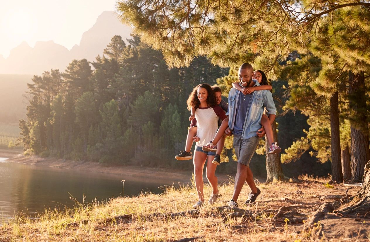 Parents Giving Children Piggyback Rides On Walk By Lake