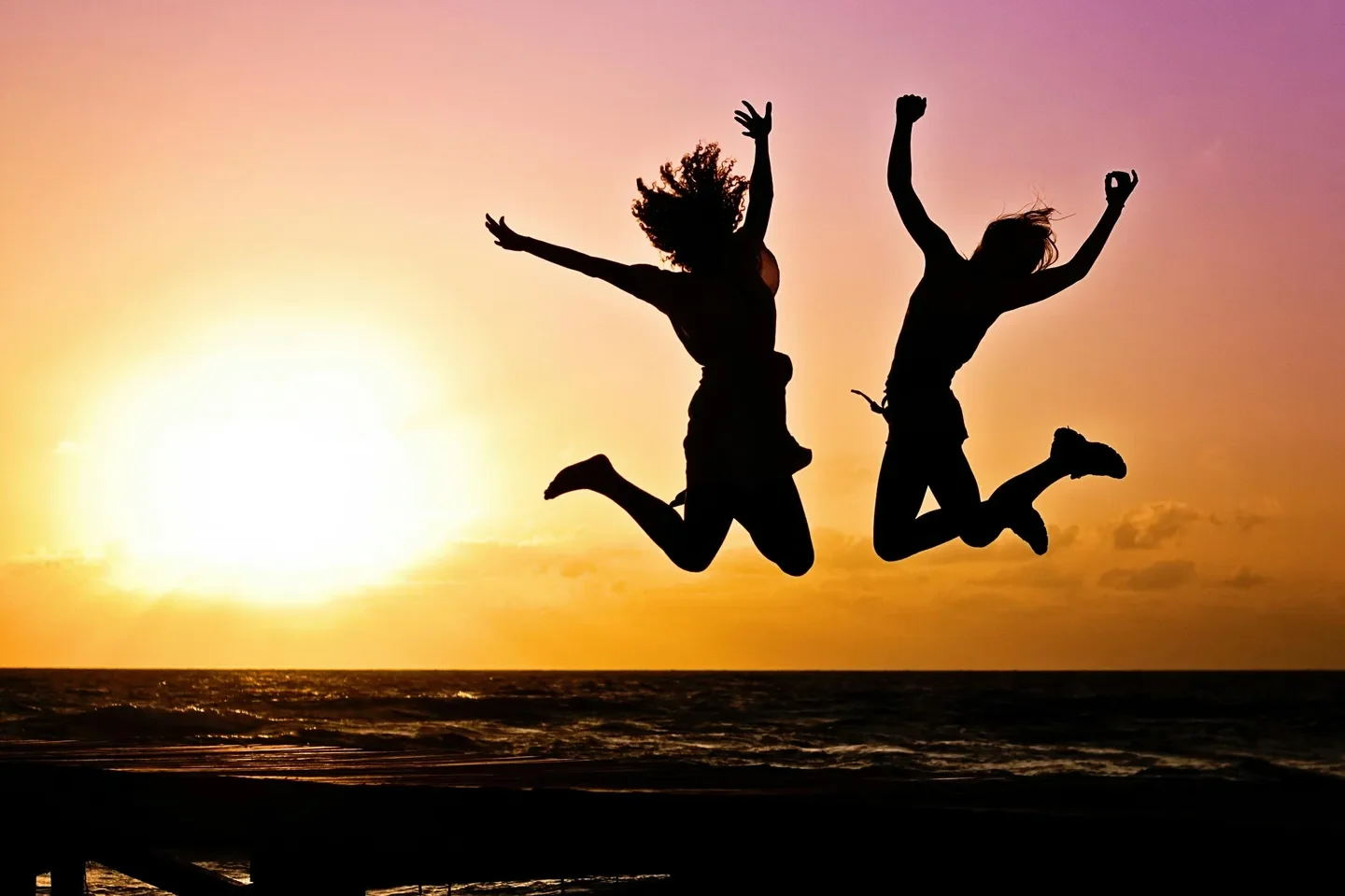 Two people jumping in the air at sunset.