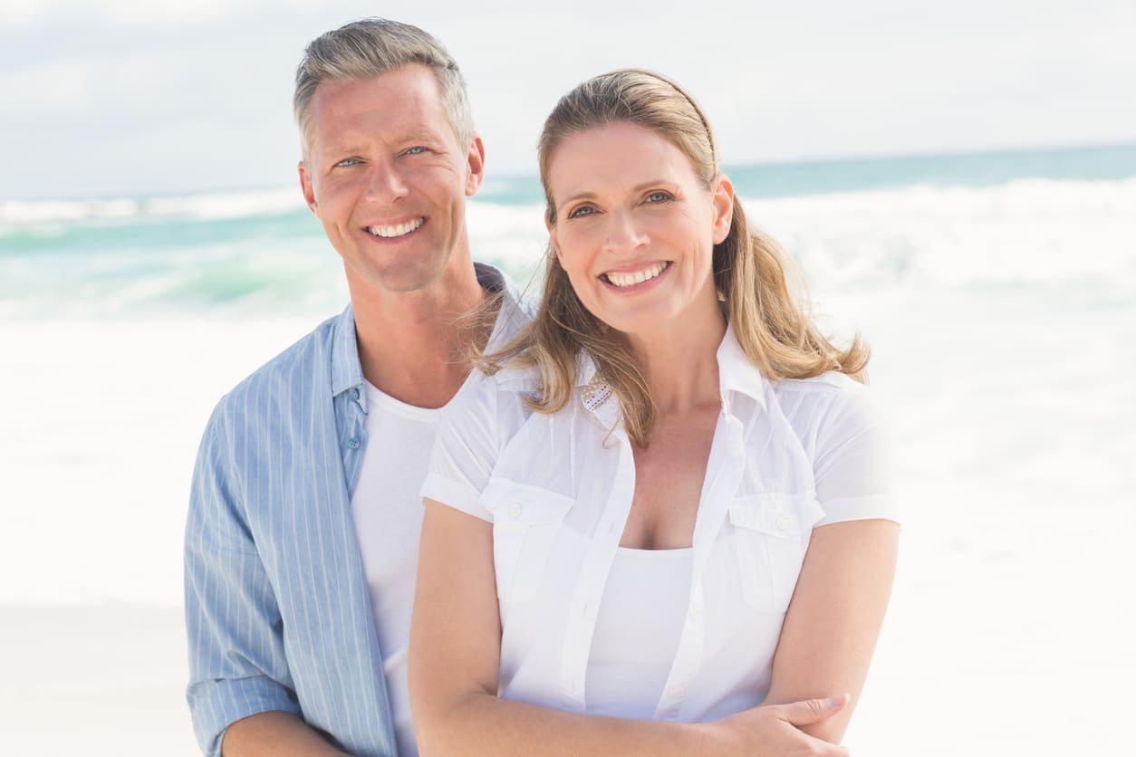 Happy couple smiling at camera at the beach